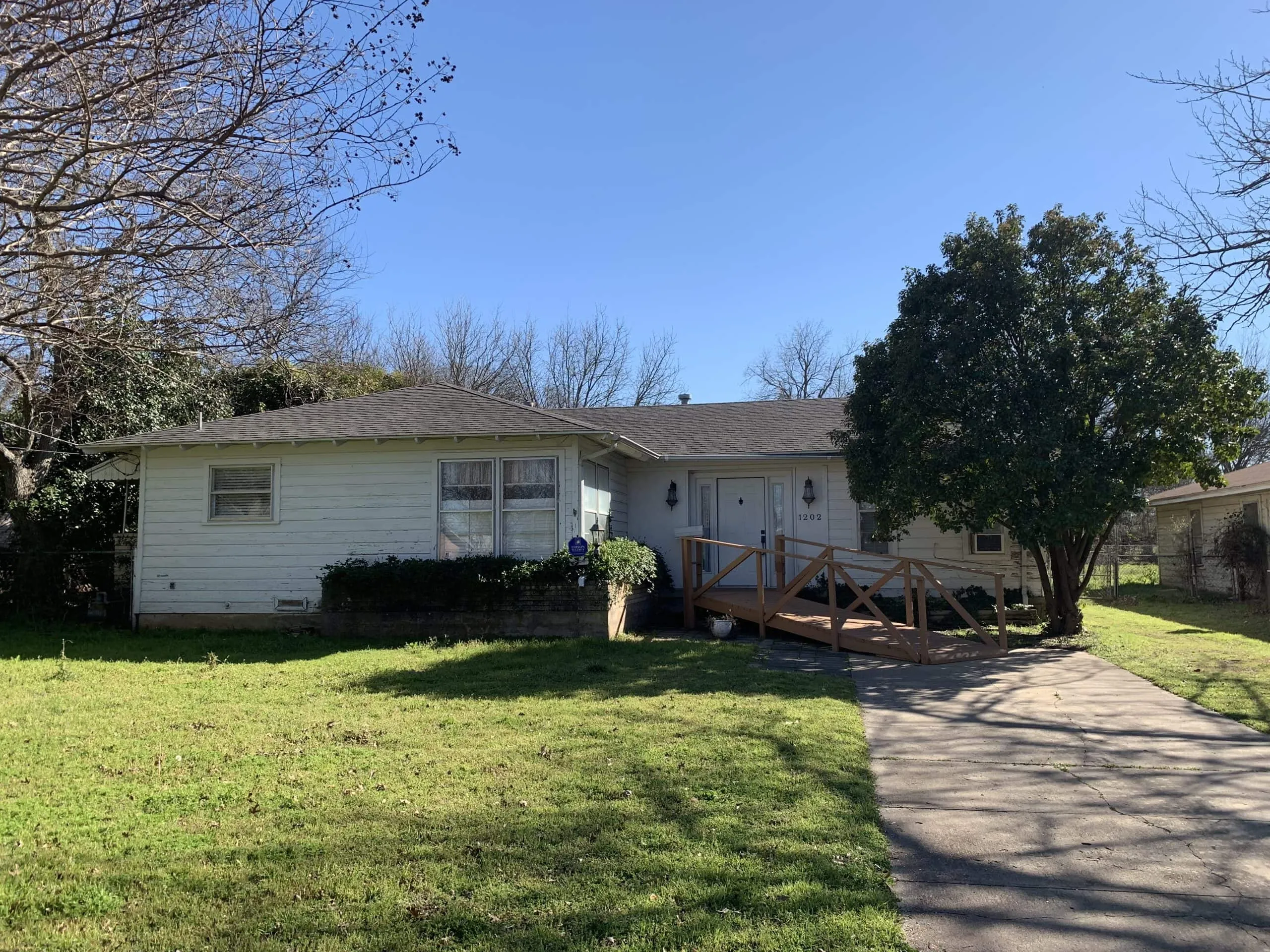 Story house with a welcoming front yard and a wooden ramp for accessibility.