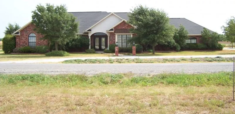 House with brick exterior, large trees, and well-maintained lawn.
